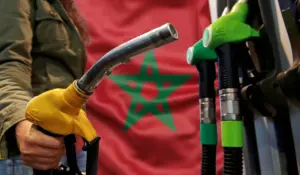 صورة قريبة لمضخة وقود في محطة توزيع بالمغرب مع العلم المغربي في الخلفية، تعبر عن انخفاض أسعار البنزين والغازوال